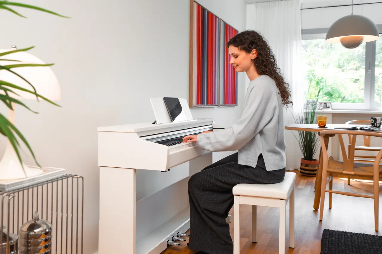 Une jeune femme joue d'un piano numérique Kawai CX blanc avec une tablette
