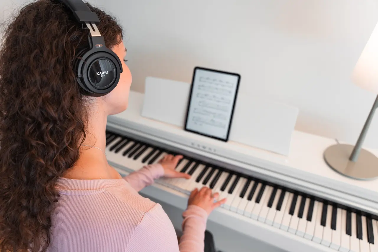 Une jeune femme avec un casque joue sur un piano numérique Kawai CX blanc