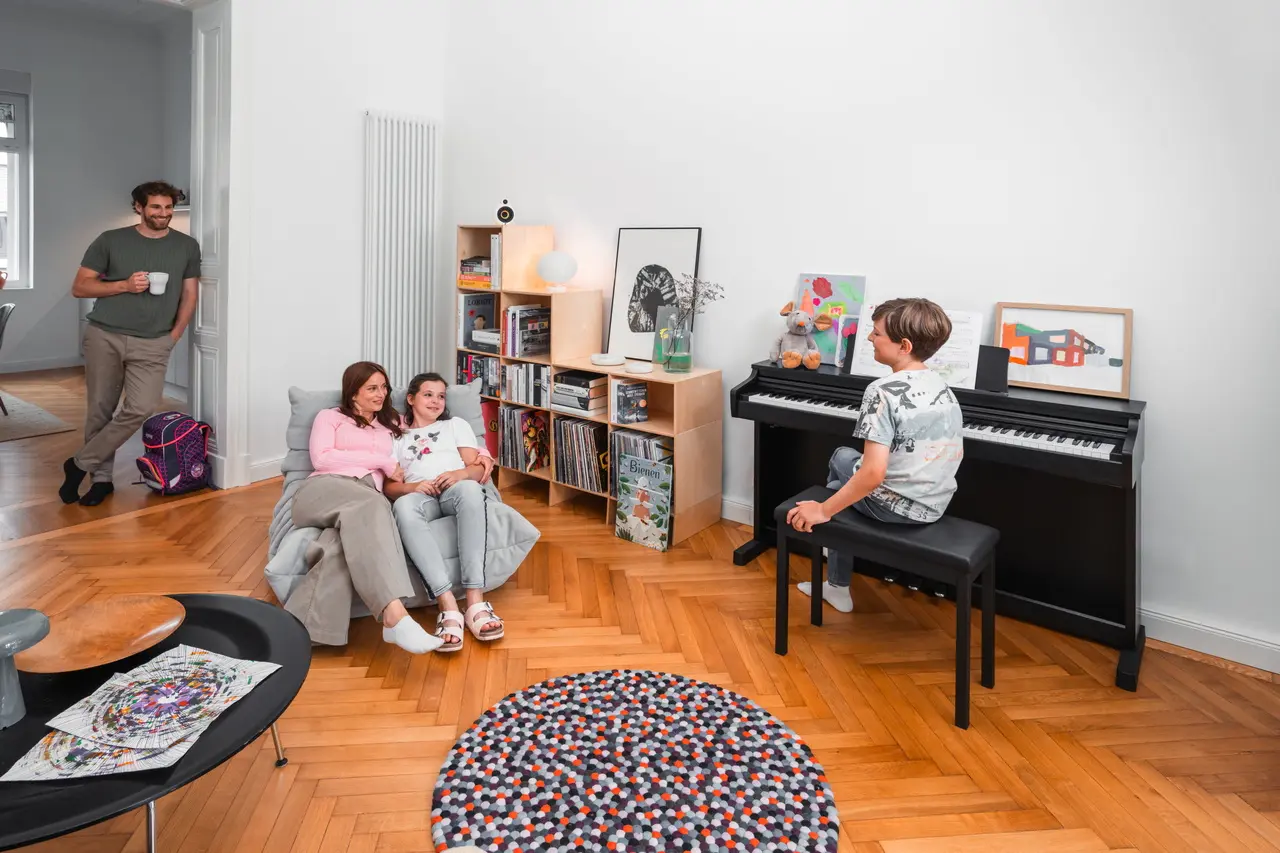 Famille dans le salon pendant qu’un enfant joue sur un piano numérique Kawai noir.