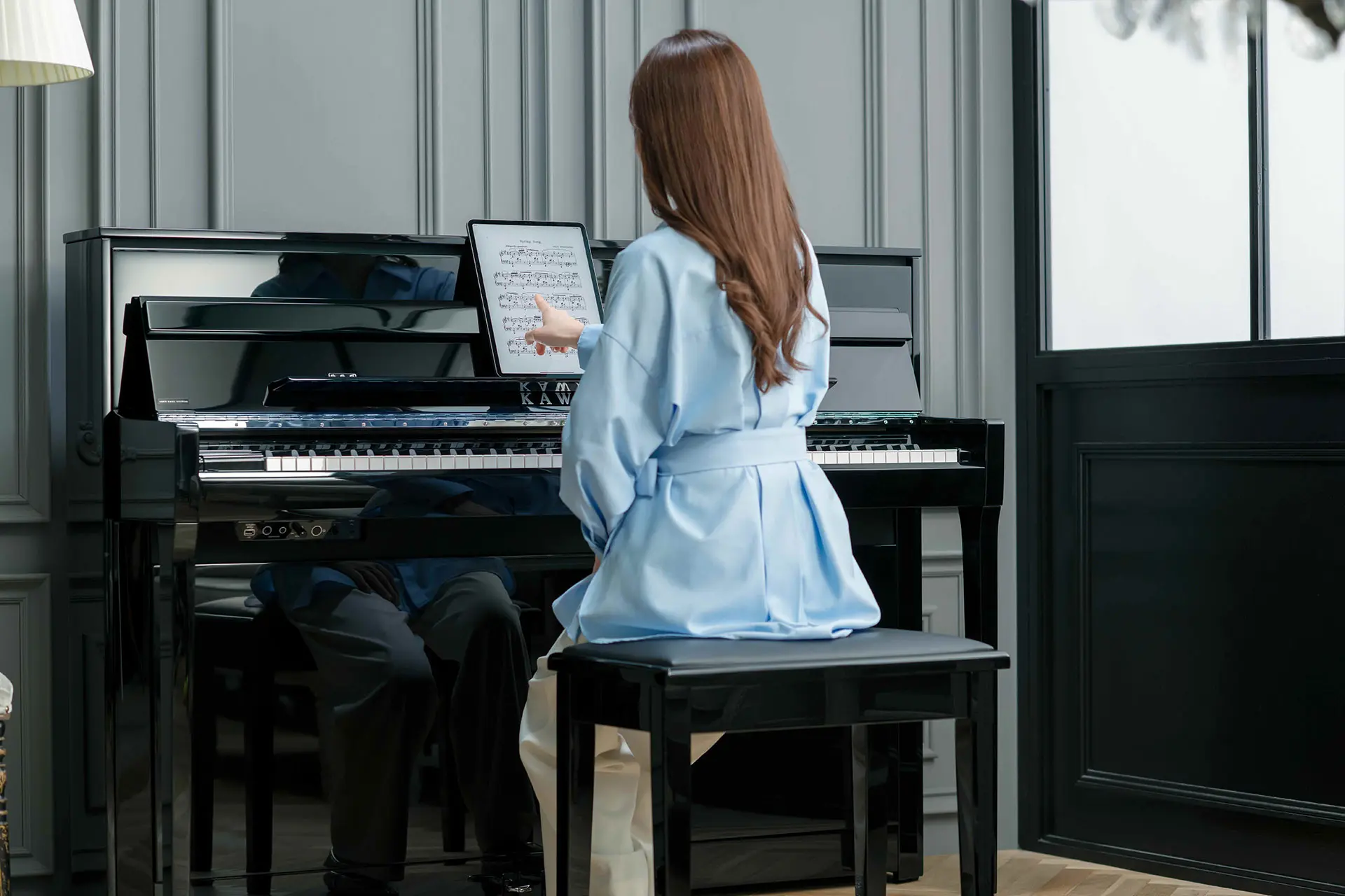 Frau sitzt am Kawai NOVUS Hybridpiano und hält ein Tablet